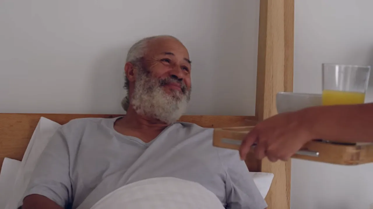 An older man smiling as breakfast is brought to him