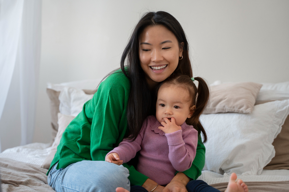 A smiling woman holding a toddler in a sunny bedroom